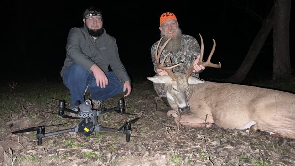Two men, a drone and a fallen buck at night